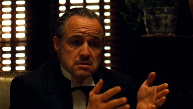 Marlon Brando sitting in a darkened room with his hands out in The Godfather