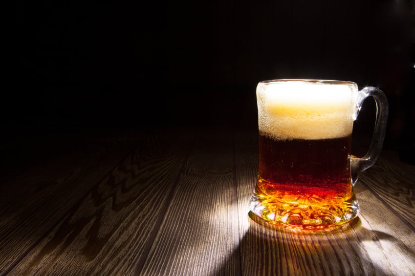 mug of beer sitting on a wooden counter in low lighting