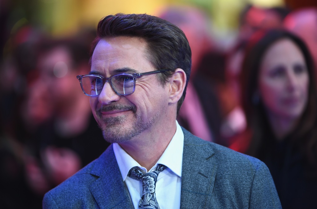 Robert Downey Jr. smiles while wearing glasses and a suit.