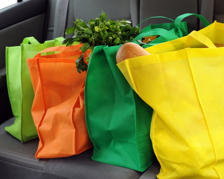 four reusable shopping bags filled with grocereis