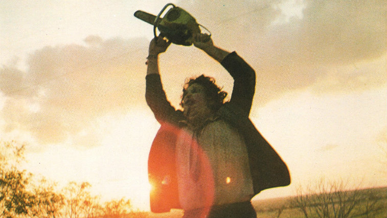Gunnar Hansen as Leatherface in The Texas Chainsaw Massacre holding a chainsaw in the air