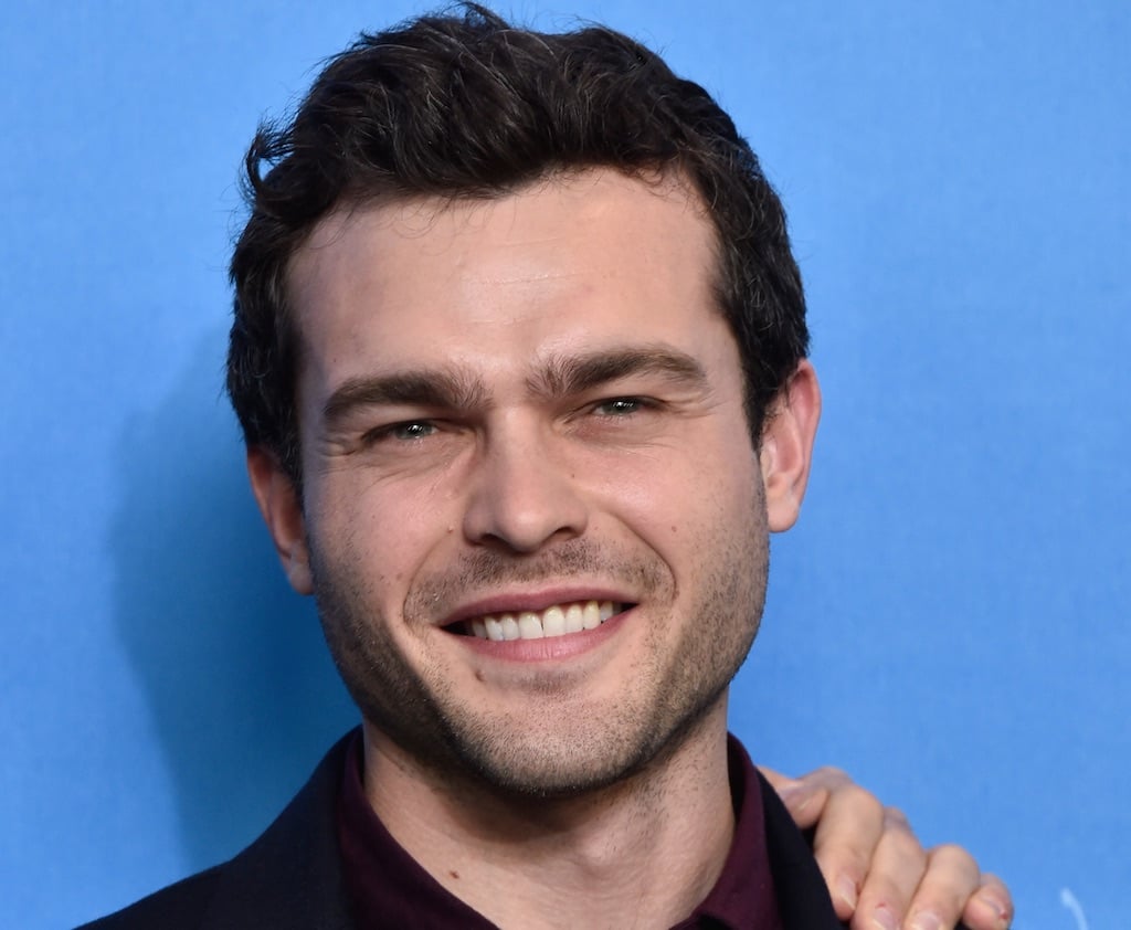 Alden Ehrenreich smiles while posing in front of a blue wall. Alden Ehrenreich smiles while posing in front of a blue wall.