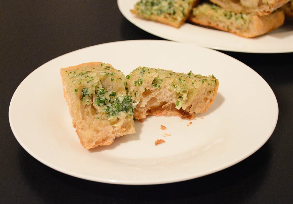 piece of buttery garlic bread with herbs on a plate that's been bitten