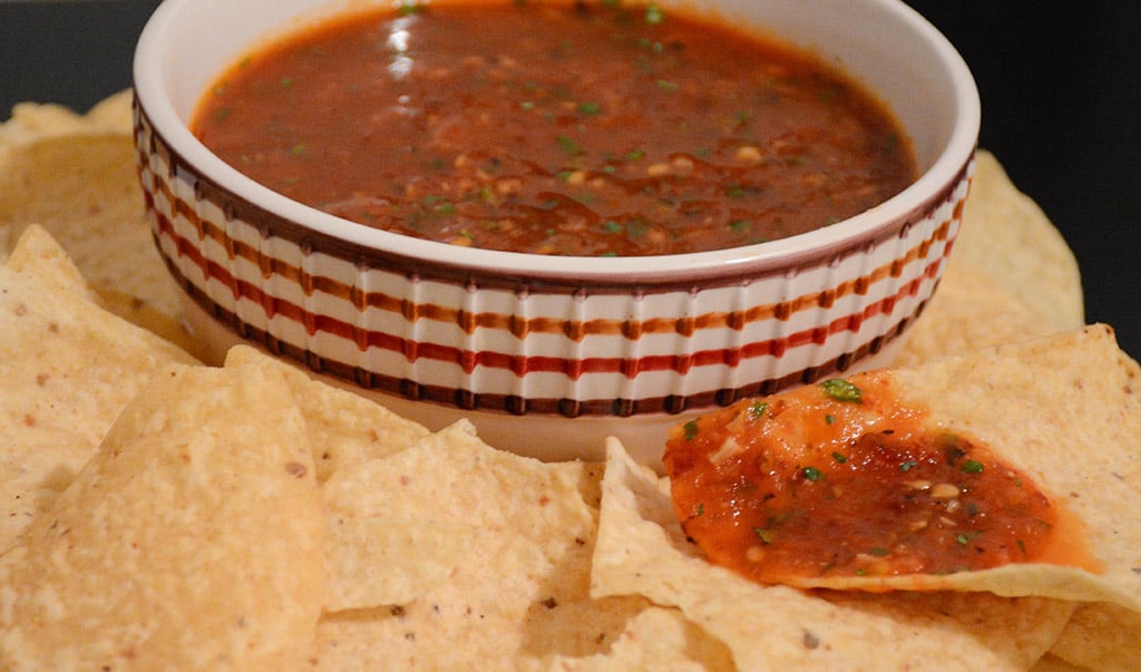 close-up of a tortilla chip dipped into smoky tomato salsa