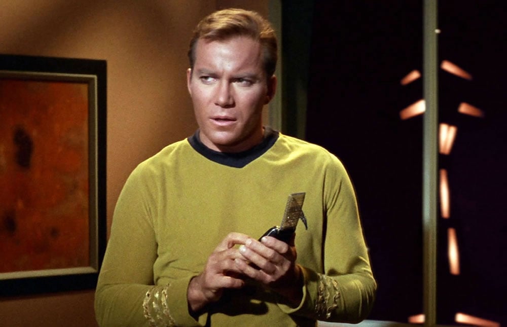 Captain Kirk looking concerned, holding a communicator with both hands