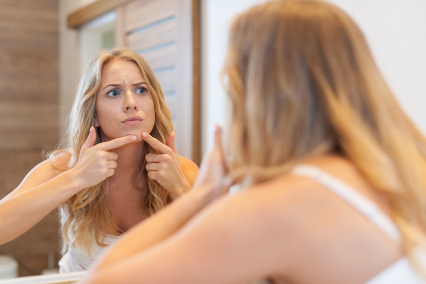 woman squeezing pimple in front of mirror