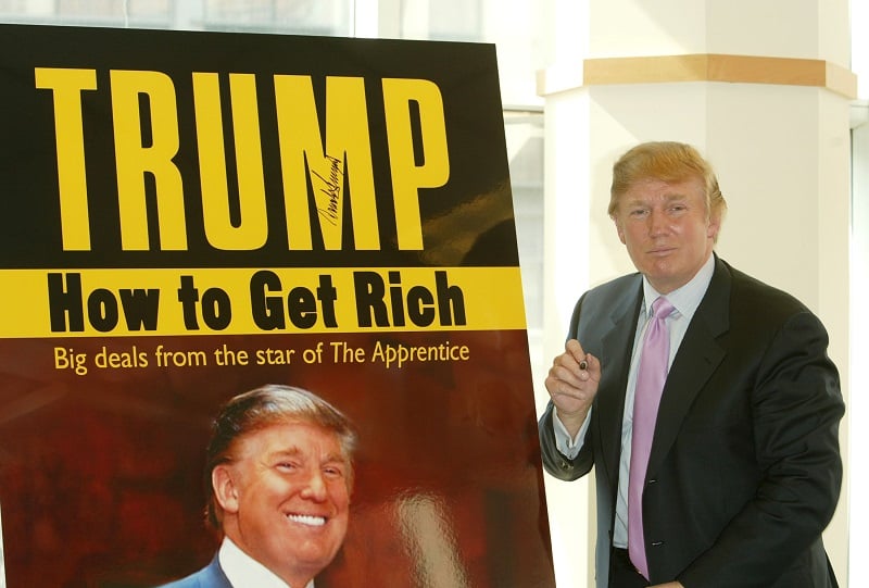 Donald Trump pauses for a moment after signing a poster depicting the over of his 2004 book "How To Get Rich"