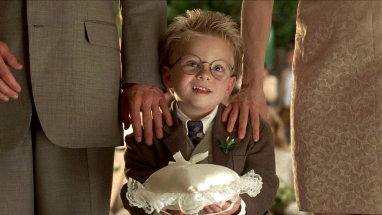 Young Jonathan Lipnicki holds a ring bearer pillow while standing between two adults in Jerry Maguire