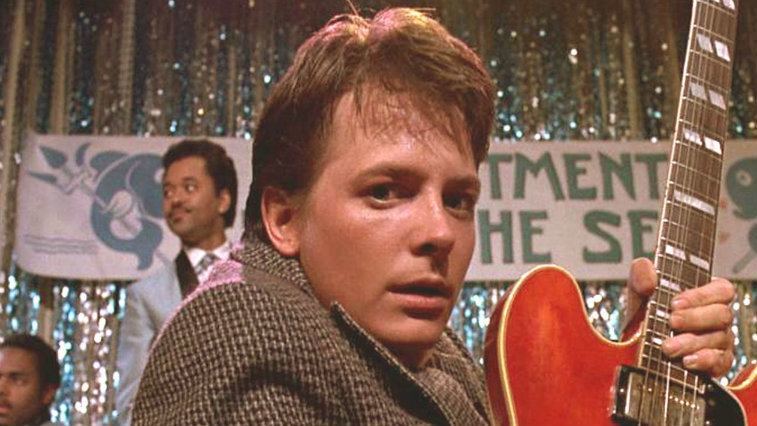 Michael J Fox playing on a guitar on stage in 'Back to the Future'.