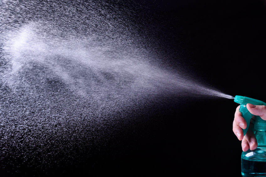 person squeezing a spray bottle over a black background