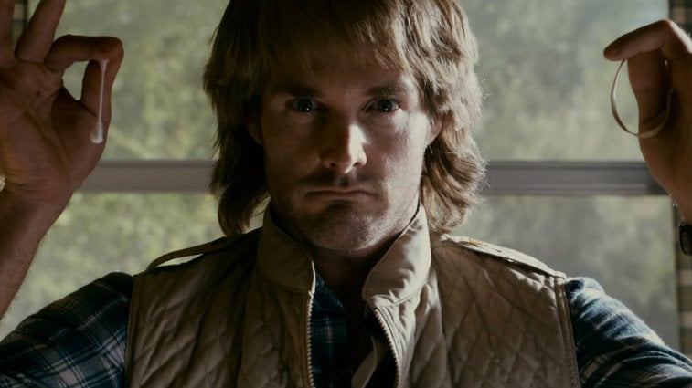 Will Forte holds up a q-tip and a rubber band in each hand in a scene from MacGruber