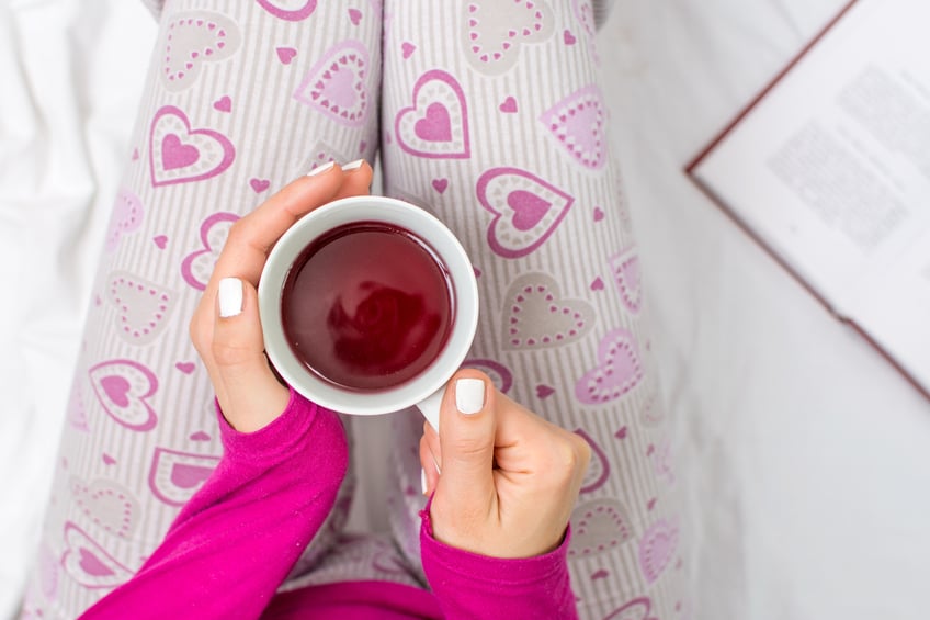 overhead image of a woman's hands holding a cup of tea in bed
