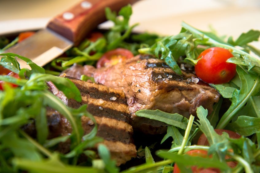 Close-up of a juicy steak served with an arugula and tomato salad