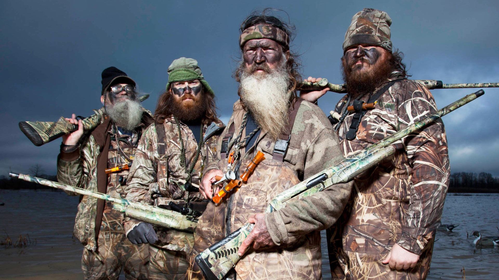 The cast of Duck Dynasty is posing together in camo and holding guns.