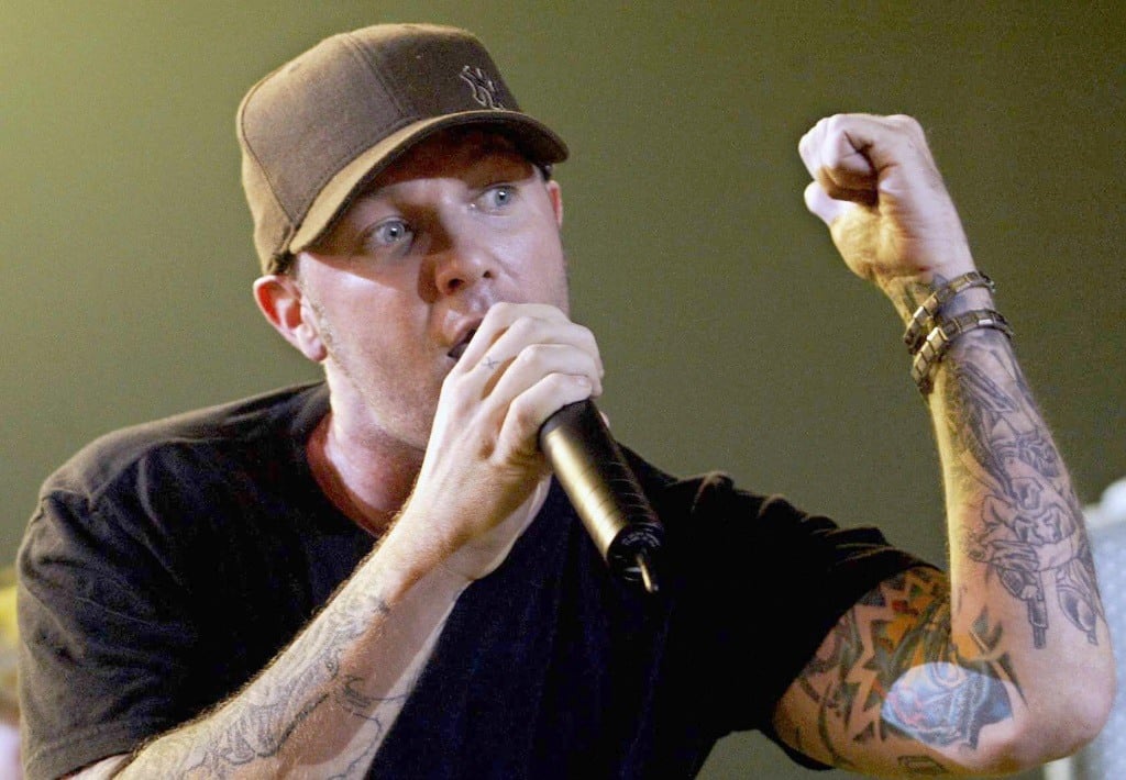 Fred Durst is rapping into a microphone while holding up a fist.