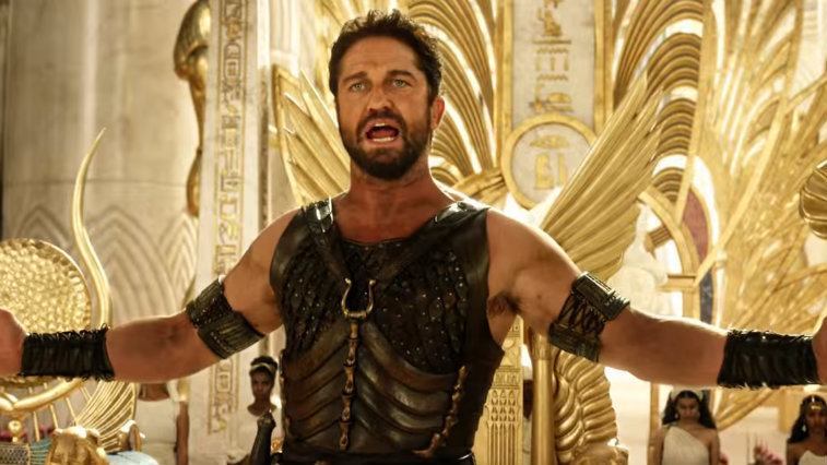Gerard Butler holds his arms out while standing in front of a golden throne in Gods of Egypt