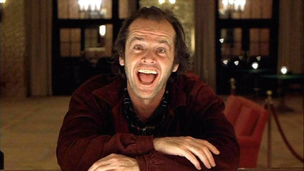 Jack Nicholson in the Shining, sitting at a bar and smiling manically