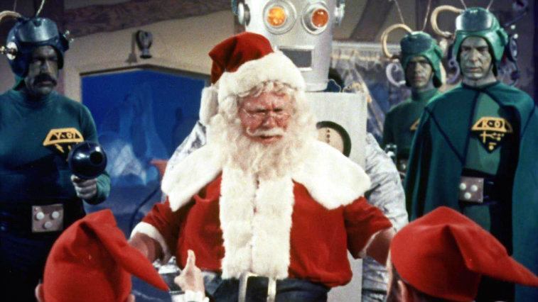 Santa Claus talks to his elves as martians look on