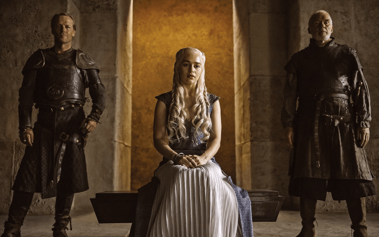 Emilia Clarke sitting next to two men on Game of Thrones.