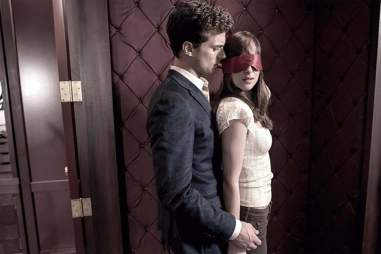 Christian Grey and stands behind a blindfolded Anastasia Steele
