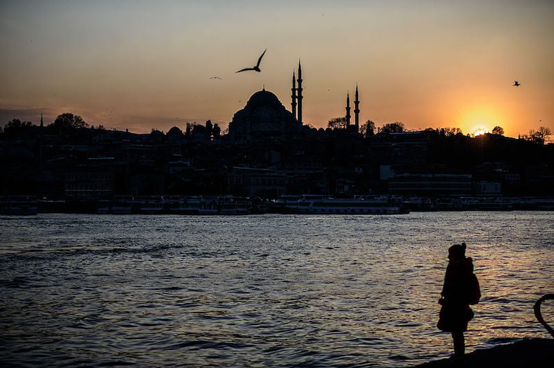 A woman stands on the shore of the Bosphorus river's Golden Horn at Karakoy district as the Suleymaniye Mosque silhouettes against the evening sky, in Istanbul on January 25, 2016. / AFP / OZAN KOSE