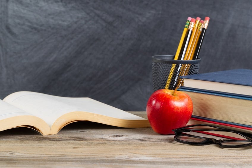 Desktop with books, red apple, reading glasses, and pencils