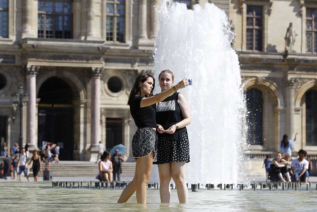 People take a selfie while wading in a fountain at the Louvre Museum