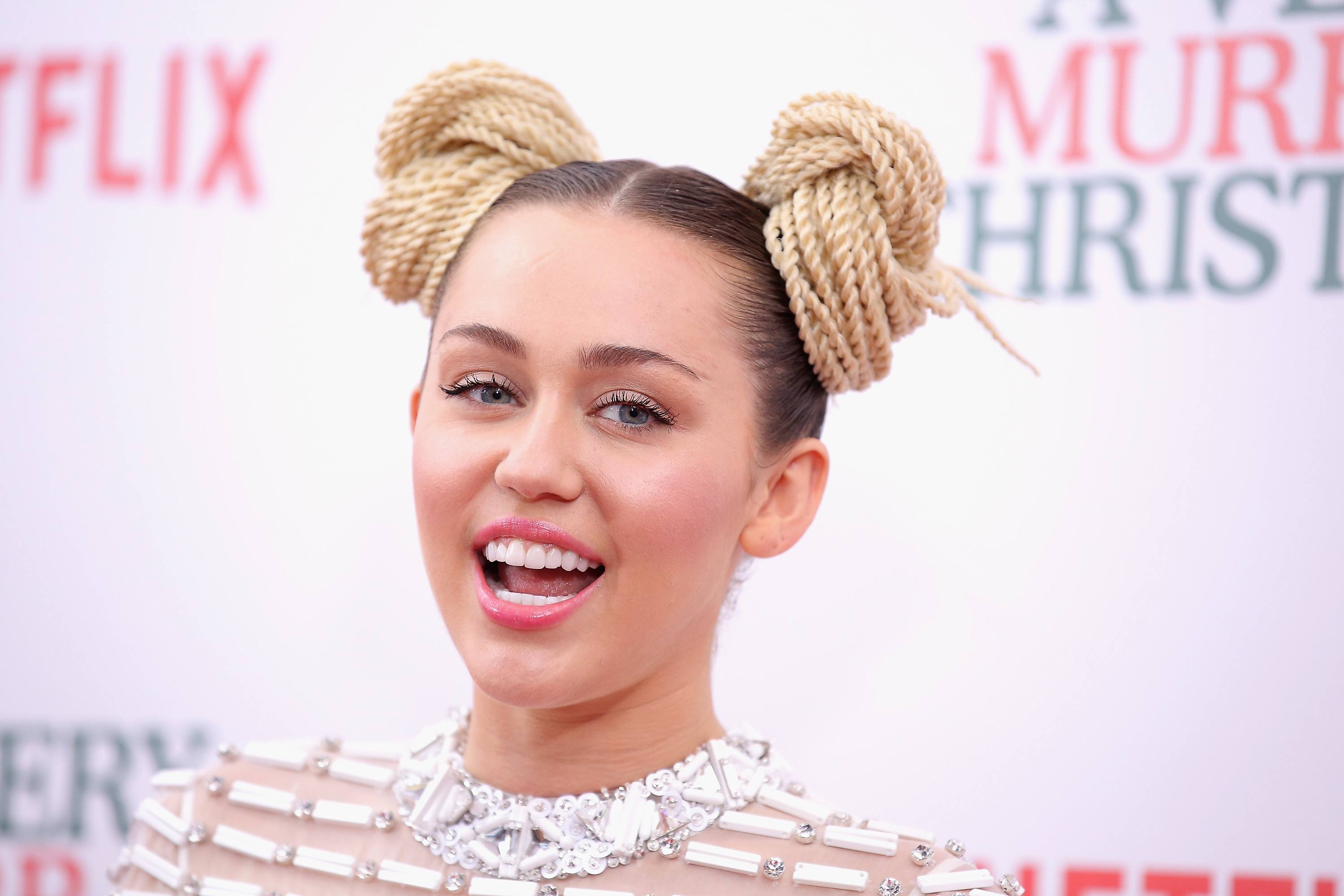 Miley Cyrus is smiling on the red carpet with two twisted hair buns.
