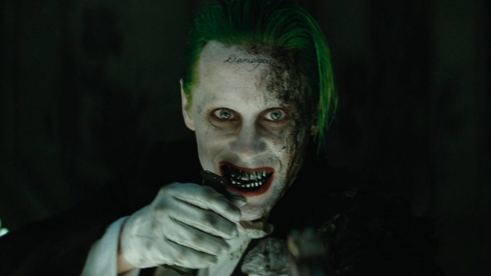 Jared Leto's The Joker raises his white gloved hand.