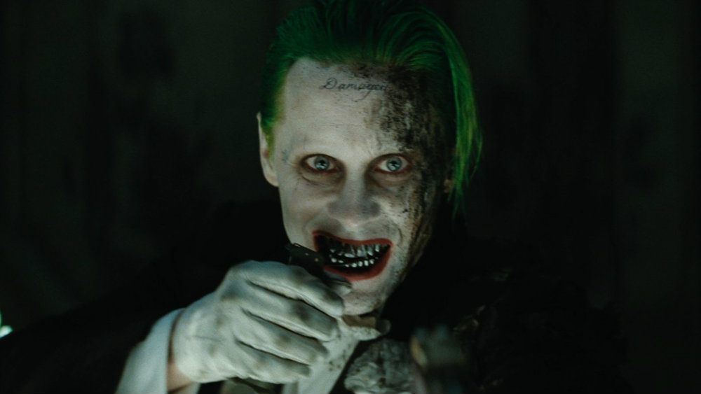 Joker smiles while holding his hand to his face. Joker smiles while holding his hand to his face.