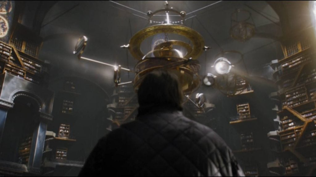 Sam Tarly, with his back to the camera looking up at a room full of golden globes and books