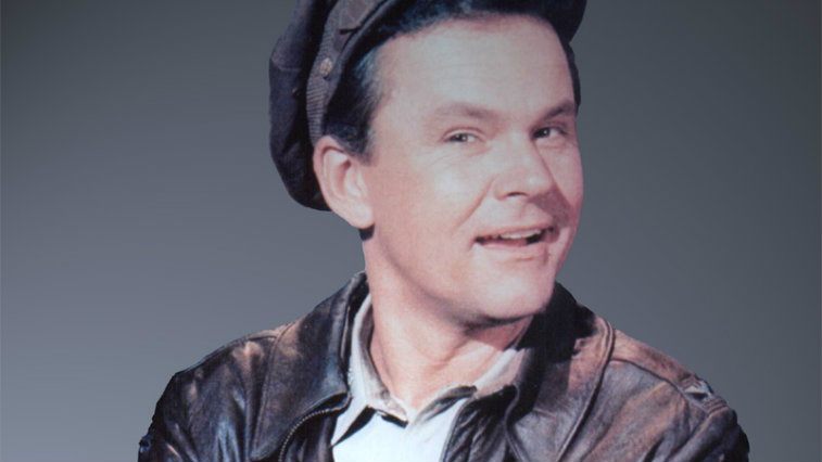 Bob Crane in 'Hogan's Heroes' smiling in front of a gray background.