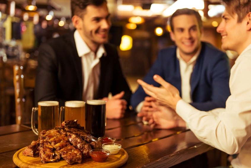 Three businessmen in suits are smiling, talking and drinking beer