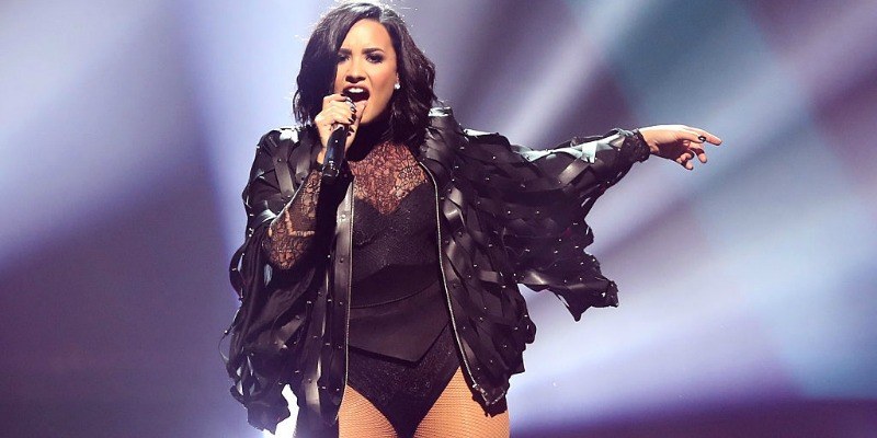 Demi Lovato sings on stage holding a microphone and wearing a leather jacket. 