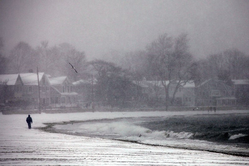 A man walks along a Connecticut beach through a snow storm