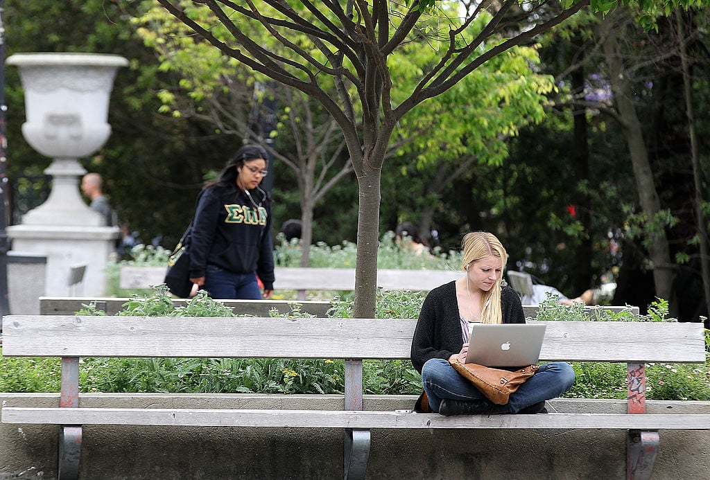 A UC Berkeley student works on her laptop while sitting on the UC Berkeley campus