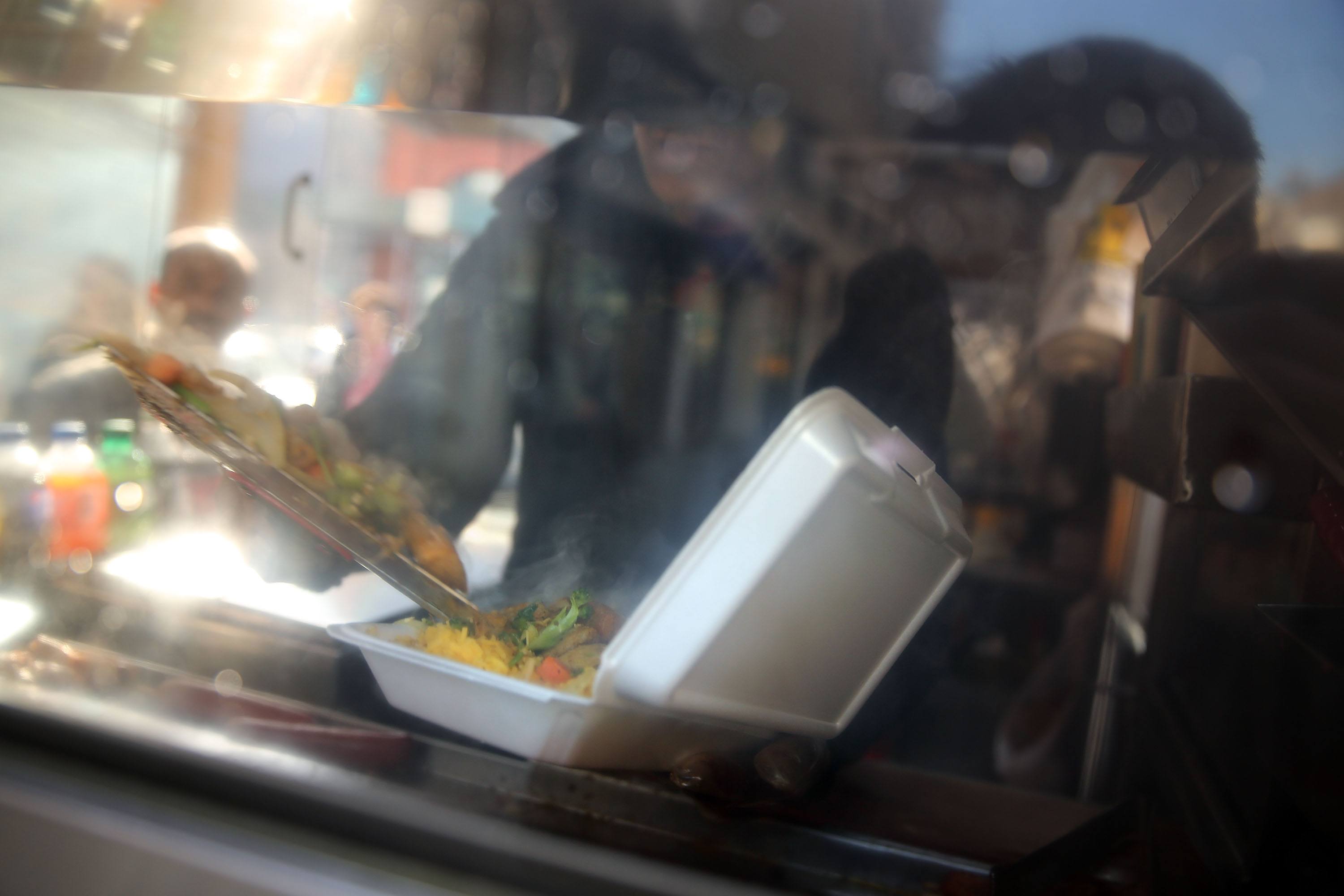 A food cart worker fills a styrofoam take-out container with food