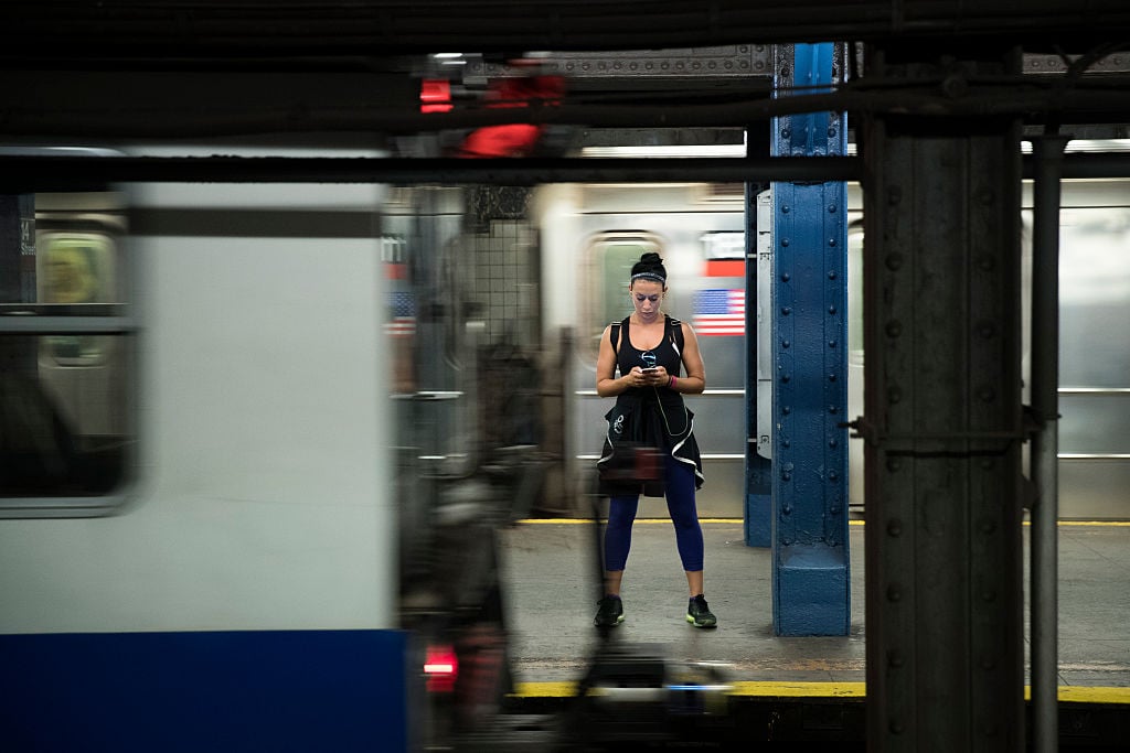 A woman looks at her smartphone as a train passes by