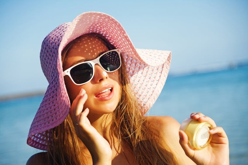 Woman wearing hat applying sunscreen