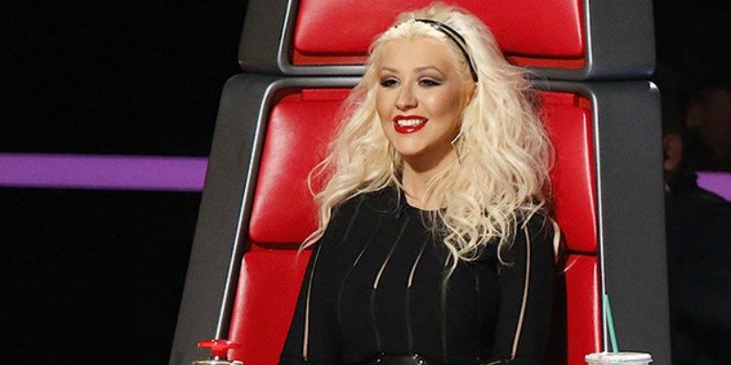 Christina Aguilera sitting in the chair and smiling on The Voice