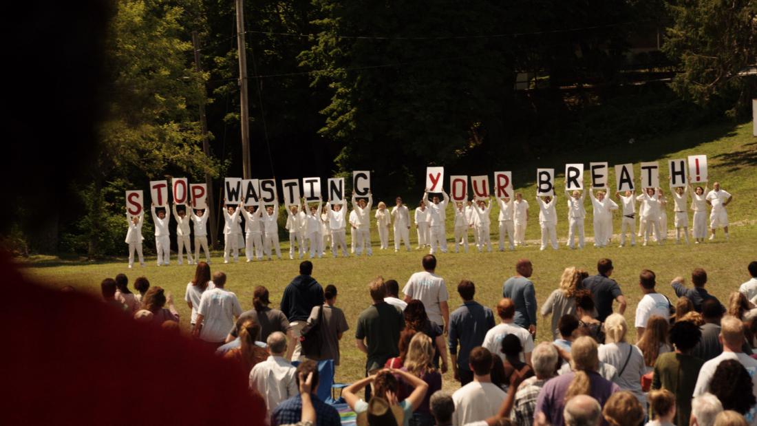 A group of protesters in white hold up signs that read Stop Wasting Your Breath in The Leftovers