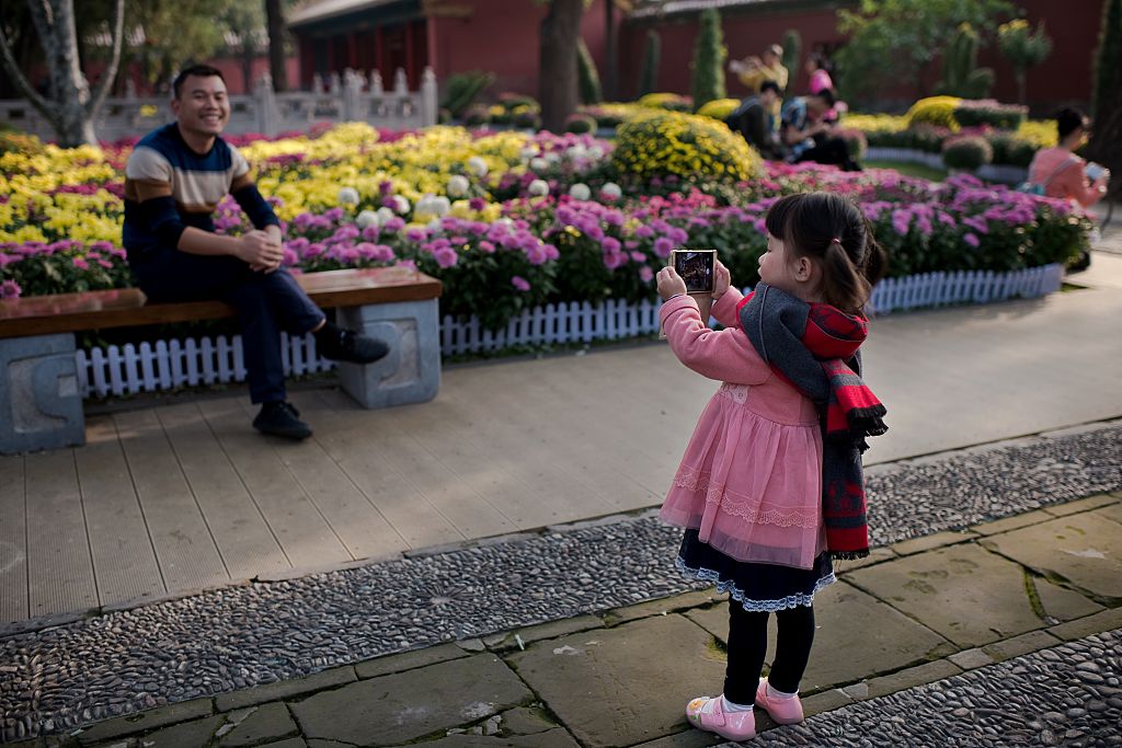 A young girl takes a photo of her dad with a smartphone
