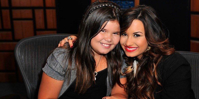 Demi Lovato and Madison De La Garza are sitting next to each other and are smiling.