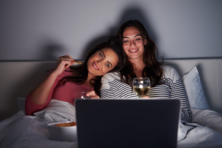 Female couple relax in bed with a laptop Female couple relax in bed with a laptop