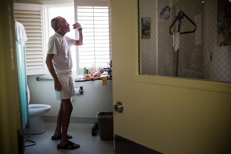An older cancer patient drinks water near a bathroom