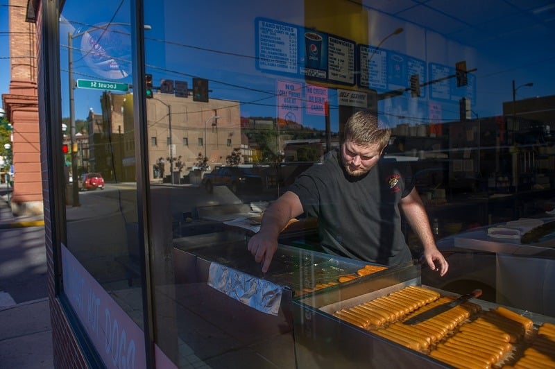 A man slowly working in a hot dog shop, perhaps feeling the effects of a loss from the previous night