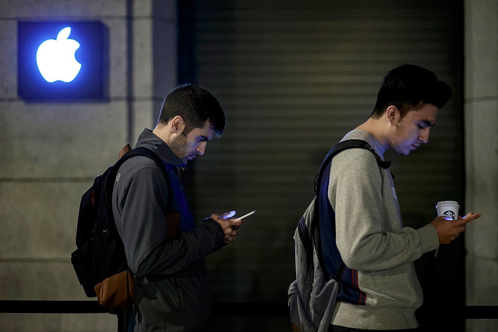 Customers check their mobile phones as they queue at Puerta del Sol Apple Store
