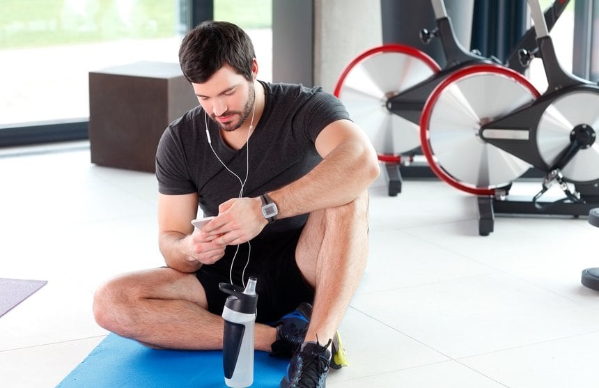 young personal trainer holding in his hand a mobile phone and listening music