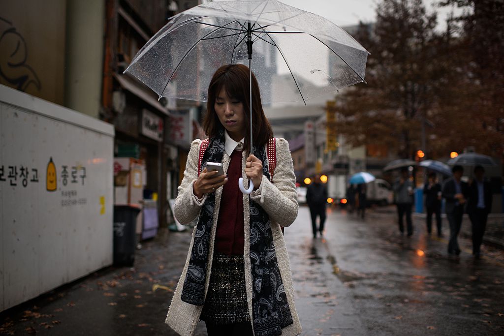 A woman uses a mobile phone as she shelters beneath an umbrella