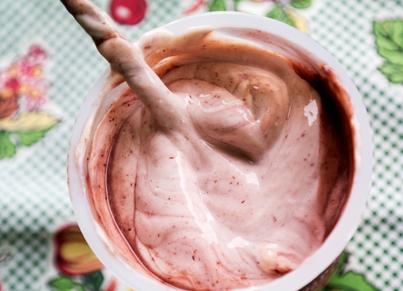 A tub of fruit flavored yogurt with a spoon on a colorful napkin